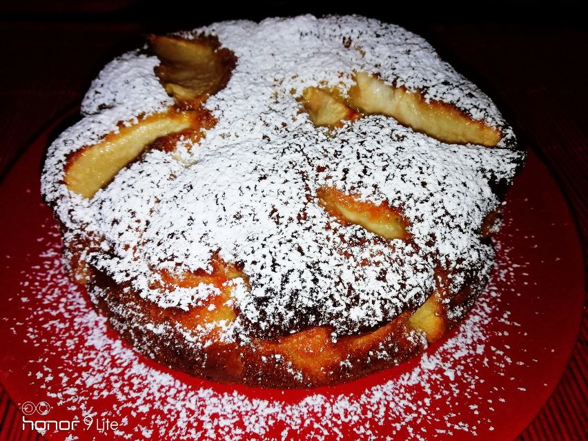 Torta di mele spolverata di zucchero a velo su un piatto rosso.